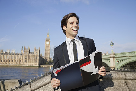 快乐的年轻商人拿着书站在英国伦敦大本钟钟楼旁