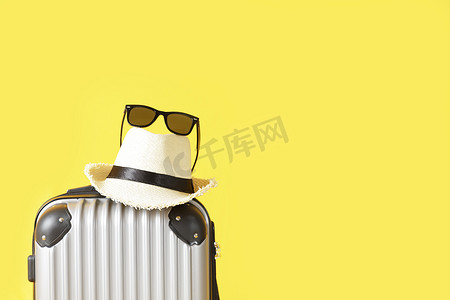 旅游黄色背景摄影照片_黄色背景上的旅行袋、行李箱、草帽和太阳镜
