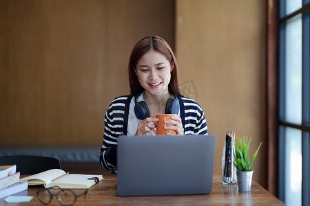 早上在图书馆上网学习时，一位年轻迷人的亚洲少女使用电脑喝咖啡的肖像
