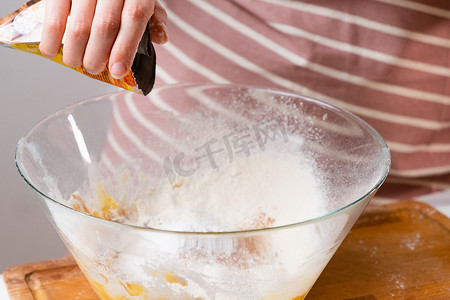 特写女人通过筛子将小麦粉筛入混合碗中，为黑色背景的蛋糕和面包店准备面团。