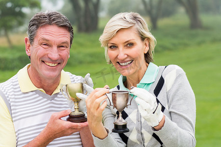 高尔夫球奖杯摄影照片_快乐的高尔夫球夫妇与奖杯