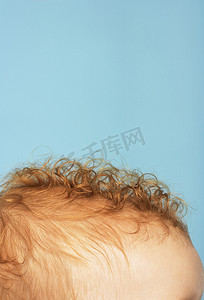 蓝色背景下红色卷发婴儿头部的裁剪图像