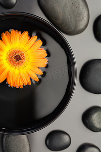 花漂浮摄影照片_橙色的花漂浮在被黑色鹅卵石包围的碗中