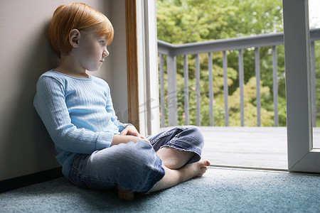 体贴的小女孩坐在家里的地毯上，透过阳台望去