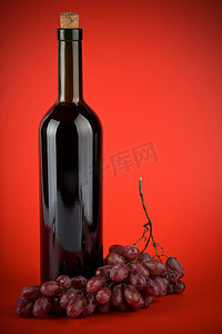 红色背景下的一瓶葡萄酒和葡萄