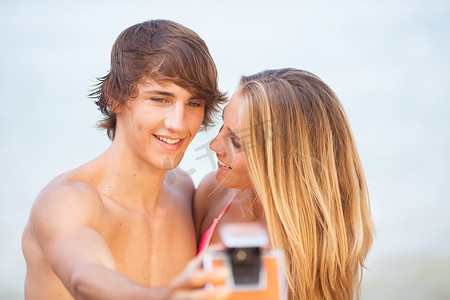 美丽的年轻夫妇在沙滩上用旧相机自拍