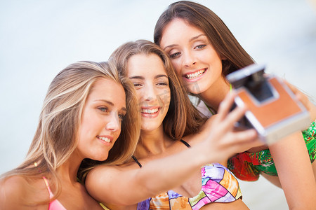 三个十几岁的美女在沙滩上用旧相机自拍