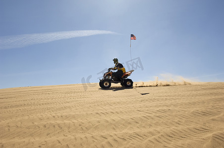 阳光明媚的日子里，一名男子在沙漠中骑四轮摩托的侧视图