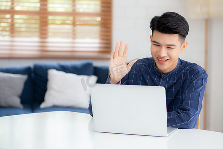 年轻的亚洲商人使用笔记本电脑进行在线视频通话打招呼并在家中交流工作，男性与笔记本开会并打招呼，社交距离，沟通理念。