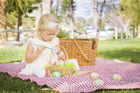 可爱的小女孩在野餐毯上给复活节彩蛋上色