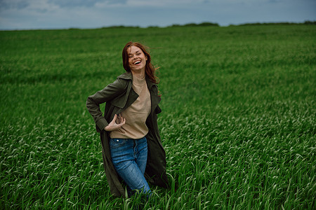 红头发、快乐的女人在雨天站在绿色的田野里。