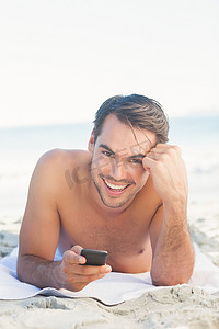 拿着他的手机的海滩的微笑的英俊的人