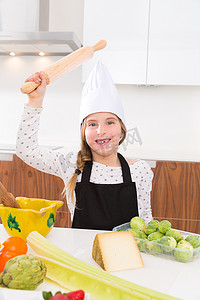 服装台摄影照片_小女孩厨师在台面上用滚轮揉捏滑稽手势