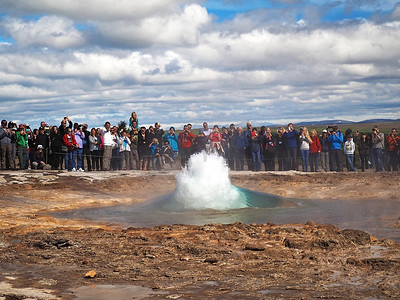 冰岛，STROKKUR，2016 年 7 月 26 日：Strokkur 间歇泉喷发黄金圈，一大群穿着五颜六色的游客拍照等待间歇泉喷发。 