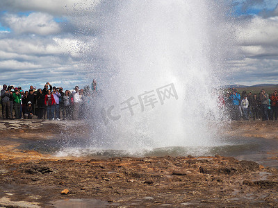 冰岛，STROKKUR，2016 年 7 月 26 日：Strokkur 间歇泉喷发黄金圈，一大群穿着五颜六色的游客拍照等待间歇泉喷发。 