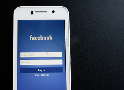 ZAPORIZHZHYA，乌克兰-2014 年 11 月 7 日： 白色智能手机与 Facebook 社交网络登录屏幕在黑桌上。