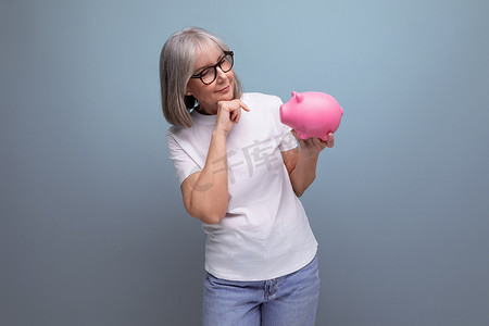 资金背景摄影照片_一位头发灰白的成年女性在工作室背景中持有存钱罐的资金，并有复制空间