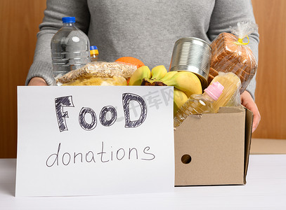 穿灰色毛衣的女人正在用纸箱包装食物，这是援助和志愿服务的概念