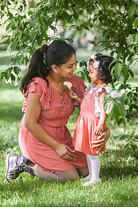 一个穿红裙的快乐女人和两岁的女孩正在春天公园里散步