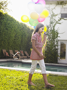一个年轻女孩带着一堆气球在草坪上行走的全长侧视图