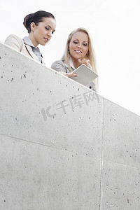 站在露台上对着天空使用数字平板电脑的年轻女性企业高管的低视角