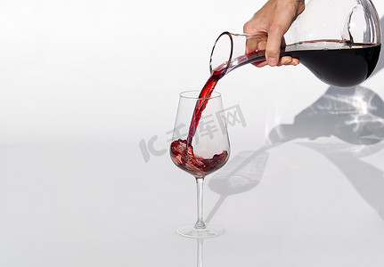 鹿酒摄影照片_侍酒师将红酒从醒酒器倒到白色背景的酒杯中。