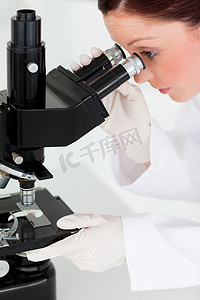 看通过显微镜的俏丽的红发科学家
