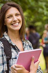 一个带着单肩包和拿着书的微笑学生的肖像