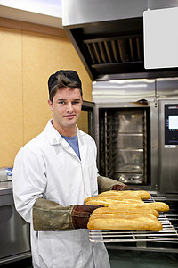 糖果展示摄影照片_快乐的面包师向站在他的镜头前展示他的法式长棍面包