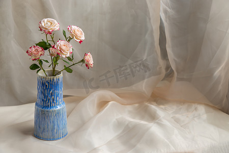 在腮红纹理桌布上的蓝色手工陶瓷花瓶中的花束。