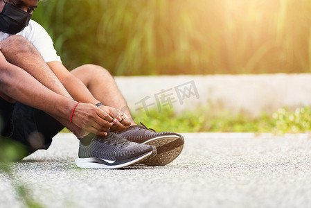 运动赛跑者黑人戴手表坐着他试鞋带跑鞋