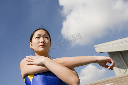 头部运动摄影照片_女运动员在多云天空下伸展手臂的低视角