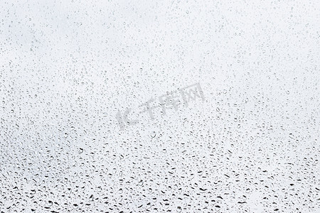 灰色天空背景下的雨滴落在窗户玻璃表面上。