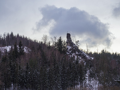 高大的砂岩，十字架和耶稣受难像在白雪覆盖的森林景观中，有雪云杉树和山丘，黄昏时田园诗般的冬季景观，蓝色小时