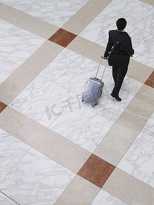 一位商人带着手提箱在瓷砖地板上行走的高视图