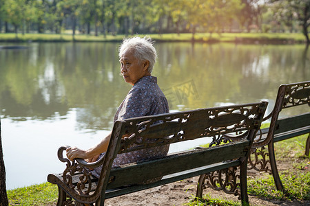 亚洲老年妇女沮丧而悲伤地坐在秋天公园的长椅上。
