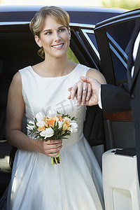 半握的手摄影照片_拿着花束的美丽新娘握着男人的手从车里下来