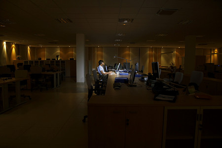一位在黑暗办公室用电脑工作的年轻女性的侧视图