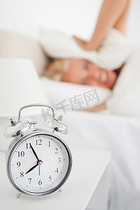 在响的闹钟摄影照片_一个女人在闹钟响时把头藏在枕头里的画像