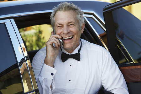 在豪华轿车开门时使用手机的快乐成熟男人