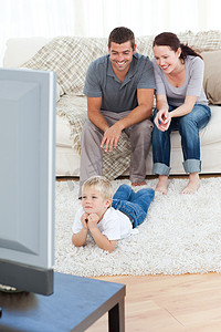 看电视的小男孩摄影照片_可爱的小男孩和他的父母在地板上看电视