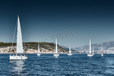 帆船比赛摄影照片_背景是帆船的美丽海景，地平线上的帆船比赛，帆船赛，激烈的比赛，鲜艳的色彩，带风车的岛屿