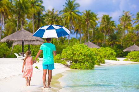 父亲和带伞的小女孩在海滩上躲避阳光