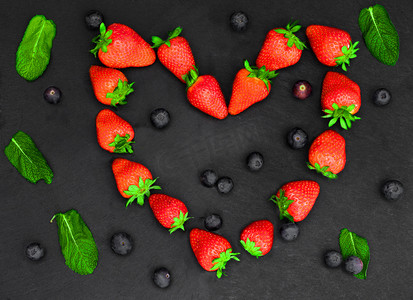 新鲜的红草莓被塑造成一颗心，排列在石板上