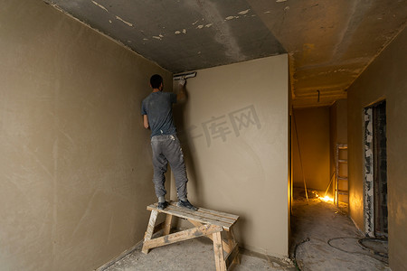 男泥水匠建筑工人正在用抹子抹灰墙。