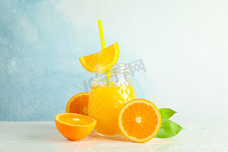 装有新鲜橙汁和小管的玻璃罐，白桌上的橙子与彩色背景，文字空间。