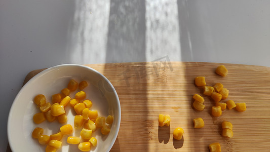 盘子里有很多黄色玉米罐头，盘子在白色背景的木竹砧板上。