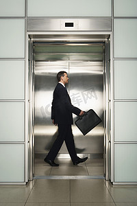 中年商人提着公文包走在电梯里的侧面照片