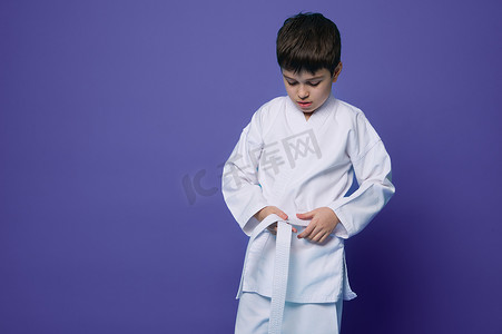 一位自信的十几岁男孩合气道摔跤手的水平肖像系着他的和服的白色腰带，在紫色背景中被隔离，带有复制广告空间