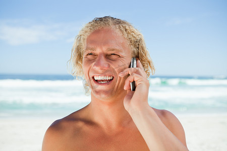 泳衣帅哥摄影照片_微笑的男人站在沙滩上用手机